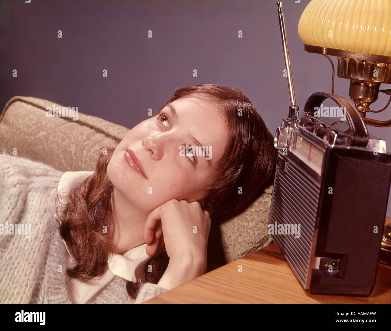 1960s TEENAGE GIRL IN LIVING ROOM CHAIR LISTENING TO PORTABLE RADIO