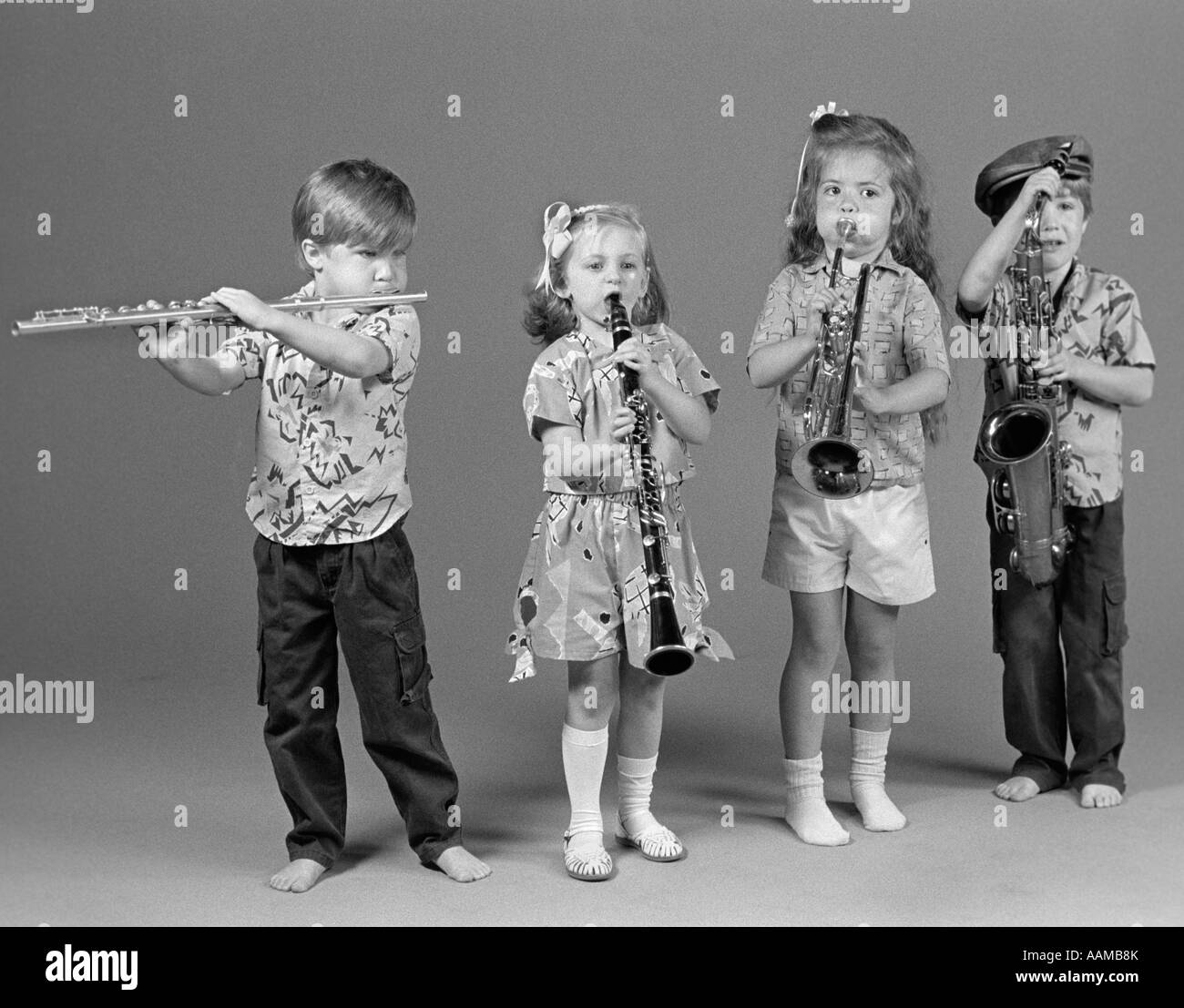 TWO BOYS AND TWO GIRLS PLAYING FLUTE CLARINET TRUMPET AND SAXOPHONE INDOOR Stock Photo