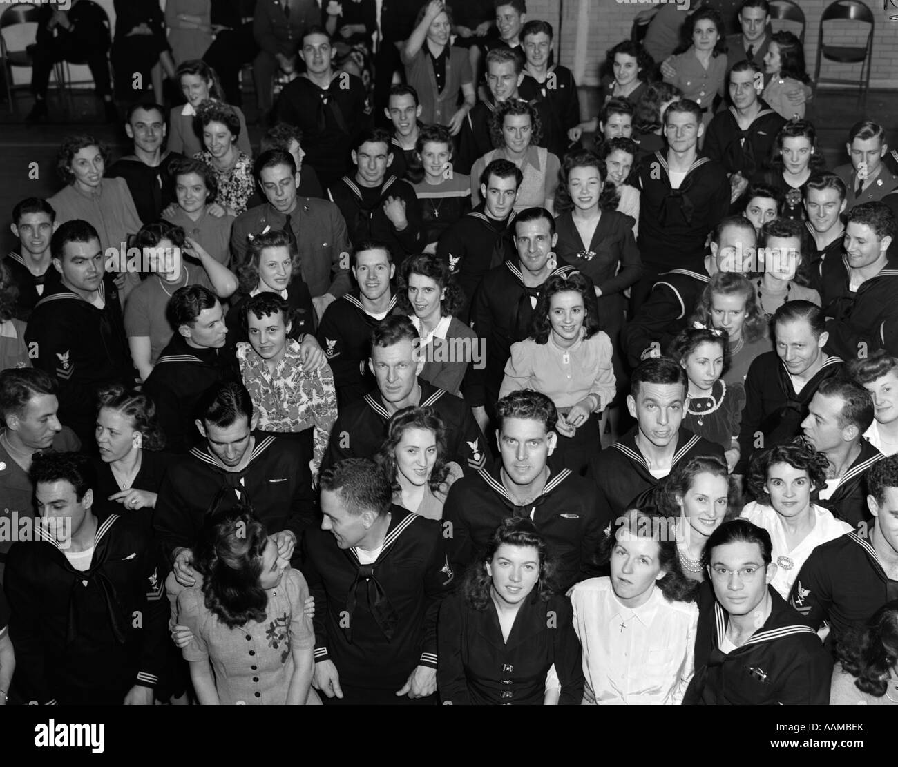 1940s CROWD MEN WOMEN CIVILIANS SOLDIERS SAILORS LOOKING UP SMILING AT CAMERA USO CENTER Stock Photo