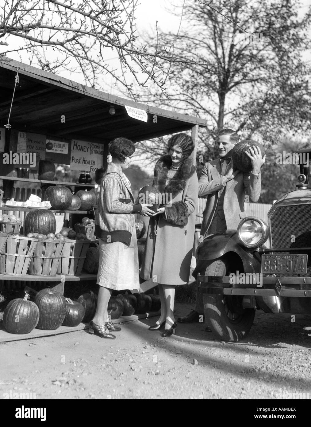 1920s COUPLE WOMEN MAN AT ROADSIDE PRODUCE STAND BUYING PUMPKINS Stock Photo