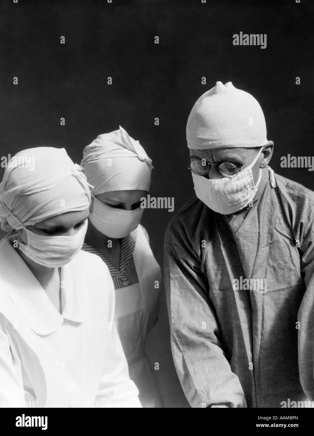1920s 1930s DOCTOR TWO NURSES WEARING SURGICAL MASKS CAPS LOOKING DOWN Stock Photo