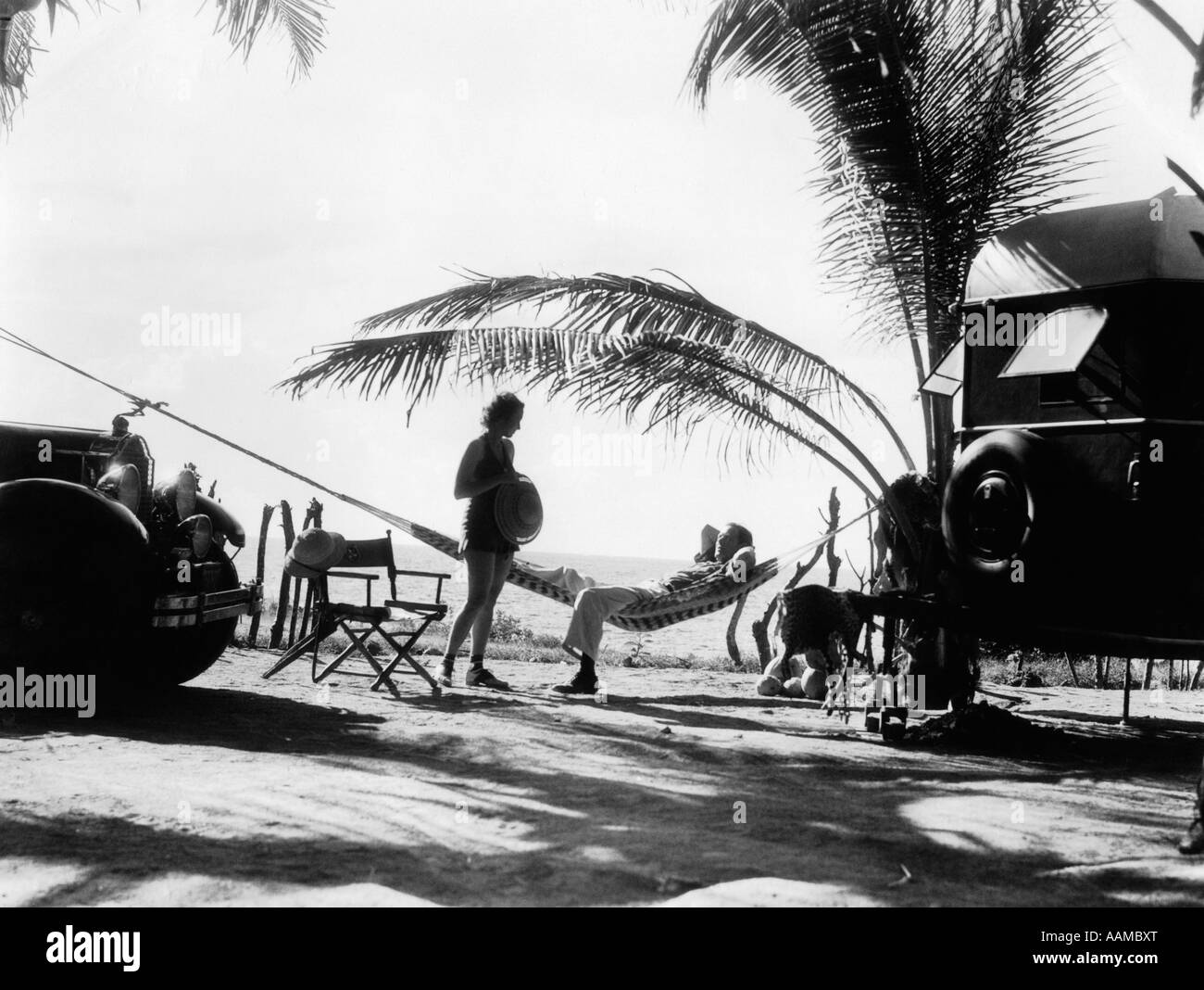 1930s COUPLE MAN WOMAN ON VACATION WITH TOURING AUTOMOBILE AND CAMPING TRAILER IN SILHOUETTE Stock Photo