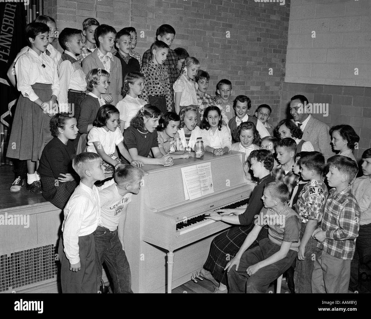 1950s GROUP SCHOOL KIDS BOYS GIRLS PIANO SINGING TEACHER PLAYS CHOIR CHORUS REHEARSAL PRACTICE SING PENN VALLEY SCHOOL Stock Photo