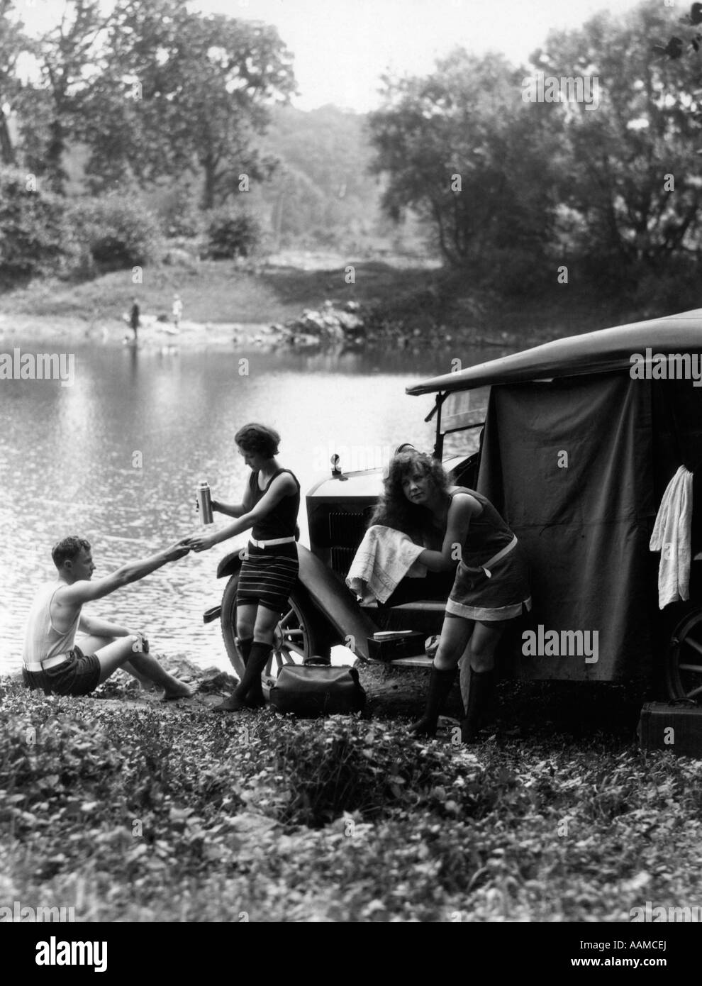 1920s GROUP OF TWO WOMEN AND ONE MAN AT LAKE WITH TOURING CAR TOWELING OFF HAIR AFTER SWIMMING Stock Photo