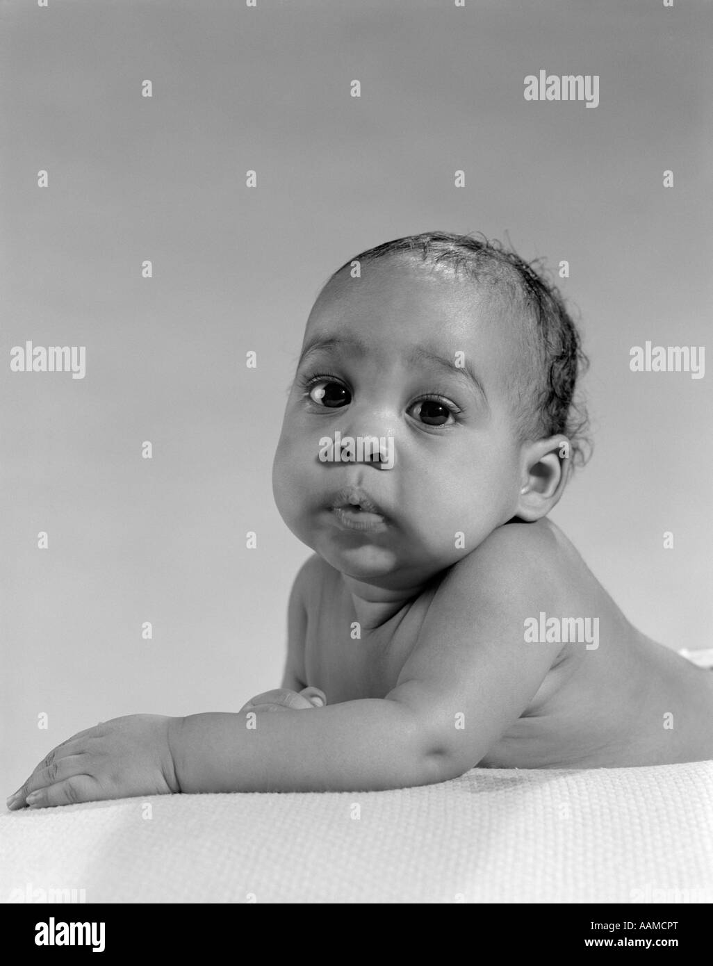 1960s PORTRAIT CHUBBY CUTE AFRICAN AMERICAN BABY LYING ON STOMACH ARMS OUT IN FRONT LOOKING AT CAMERA Stock Photo