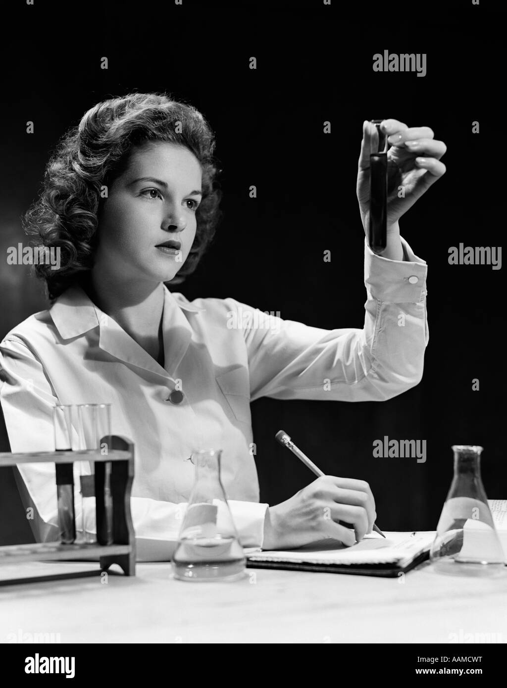 1940s STUDENT NURSE HOLDING UP TEST TUBE WHILE TAKING NOTES IN SCIENCE CLASS Stock Photo