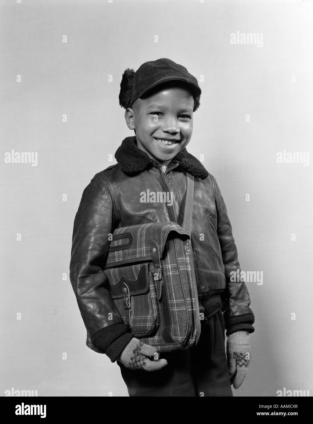 1940s 1950s AFRICAN AMERICAN BOY SMILING WEARING WINTER JACKET GLOVES HOLDING SCHOOL BOOK BAG Stock Photo