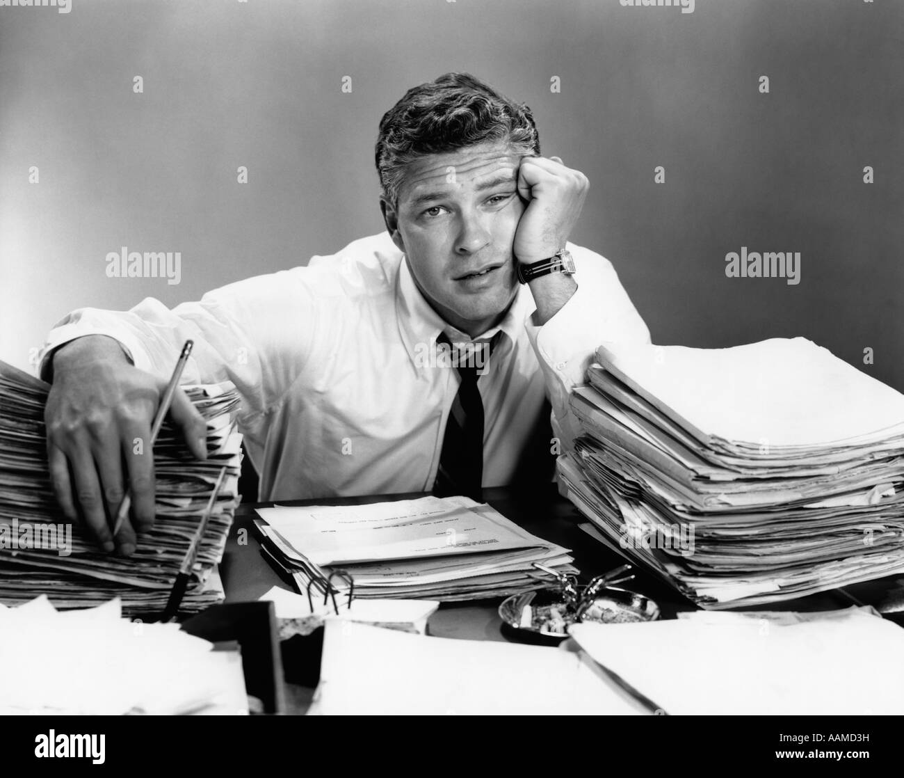 1950s PORTRAIT MAN OVERWORKED WITH DESK FULL OF PAPERS Stock Photo