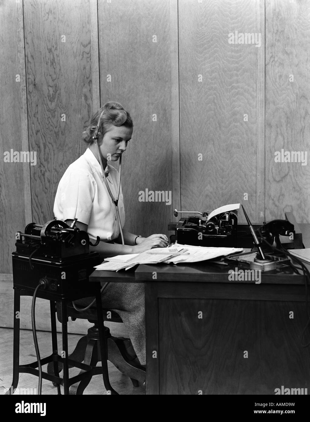 1930s WOMAN SECRETARY AT BUSINESS OFFICE DECK TRANSCRIBING FROM DICTAPHONE DICTATION VOICE RECORDING MACHINE Stock Photo