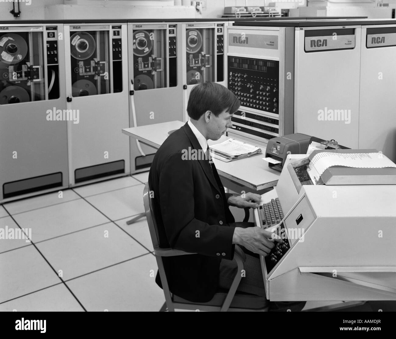 1960s SIDE VIEW OF MAN IN JACKET & TIE OPERATING LARGE COMPUTER TERMINAL Stock Photo