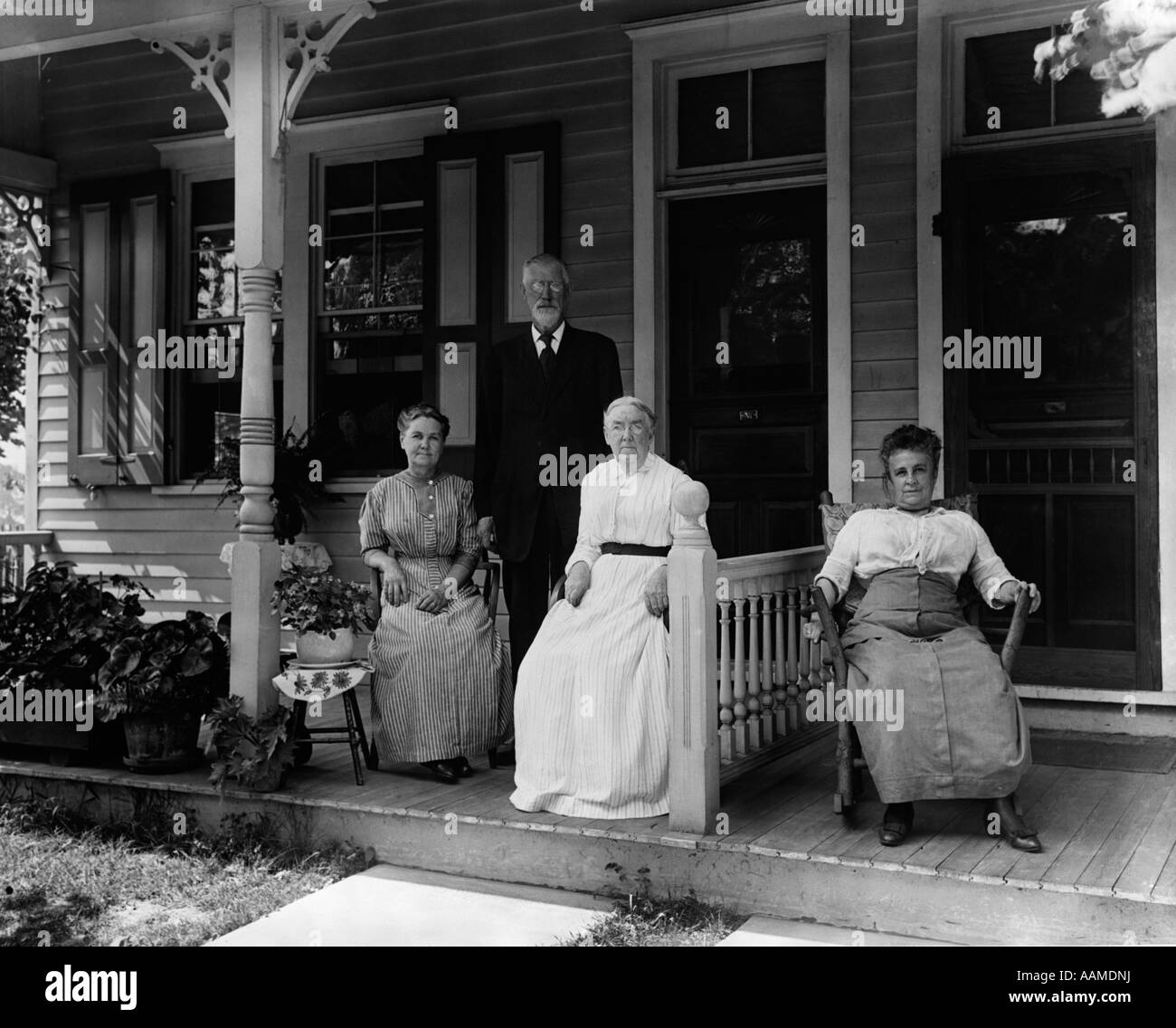 1890s 1900s TURN OF THE CENTURY GROUP OF FOUR NEIGHBORS SITTING ON THE PORCH OF A DUPLEX Stock Photo