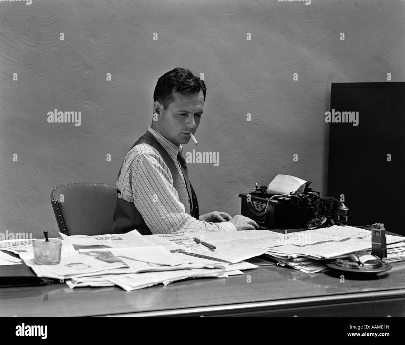 1930s 1940s BUSY MAN IN SHIRT SLEEVES BEHIND OFFICE DESK WORKING AT TYPEWRITER SMOKING CIGARETTE Stock Photo