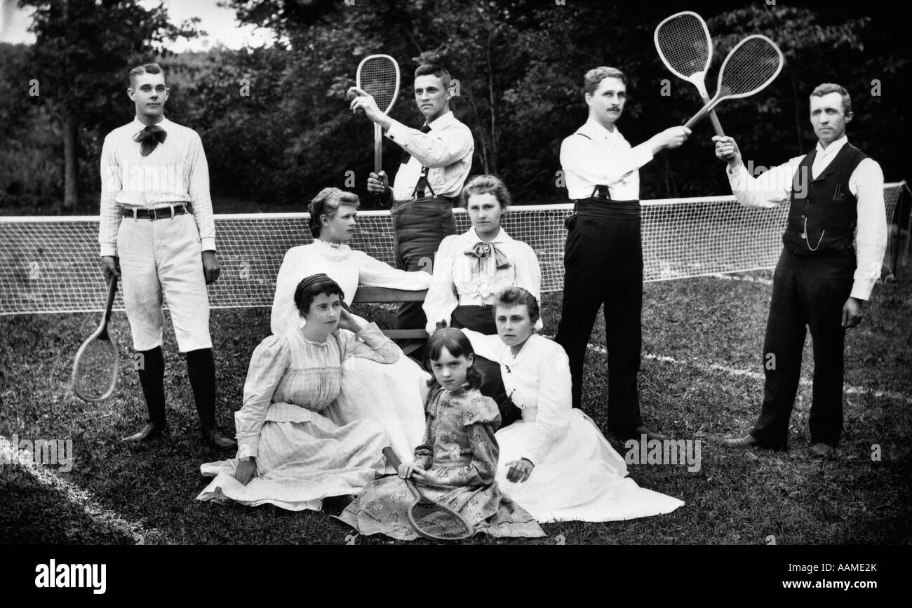 1890s TURN OF THE CENTURY GROUP PORTRAIT OF MEN HOLDING RACQUETS & WOMEN & ONE CHILD IN FRONT OF NET ON GRASS TENNIS COURT Stock Photo