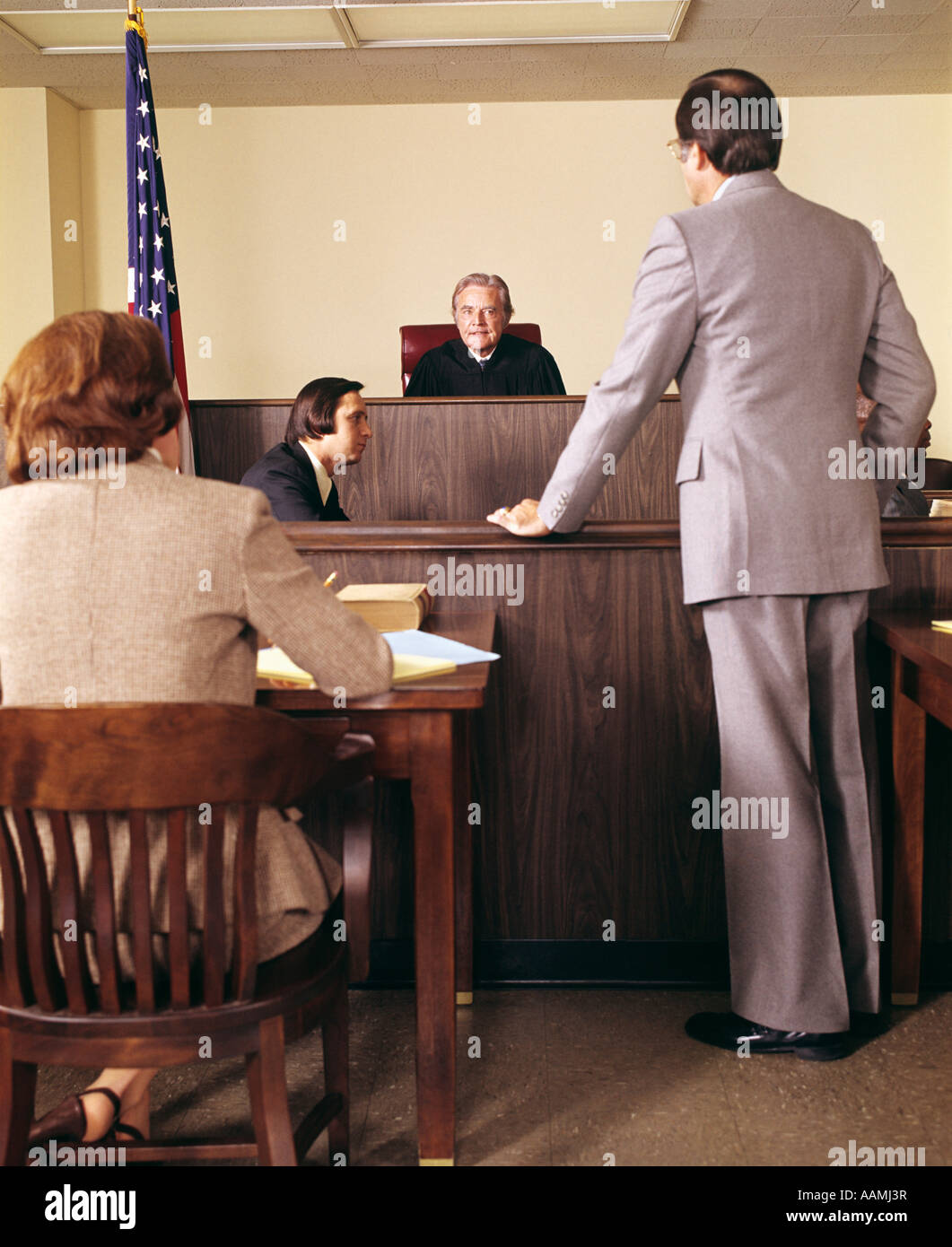 1970s COURTROOM JUDGE ON BENCH LISTEN TO ATTORNEY MAN PLEAD CASE STANDING WOMAN LAWYER SIT AT DESK LAW LEGAL COURT Stock Photo