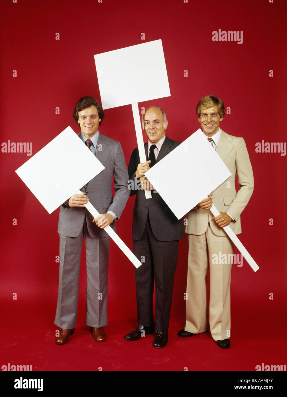 1970s THREE BUSINESSMEN HOLDING UP PICKET SIGN BOARDS SYMBOLIC MAN Stock Photo