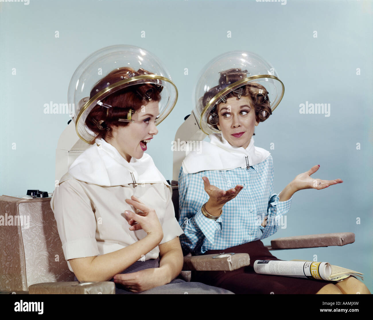 1960s 2 WOMEN SIT UNDER BEAUTY SALON HAIR DRYERS CLEAR HELMETS HOODS CURLERS TALKING GOSSIP Stock Photo