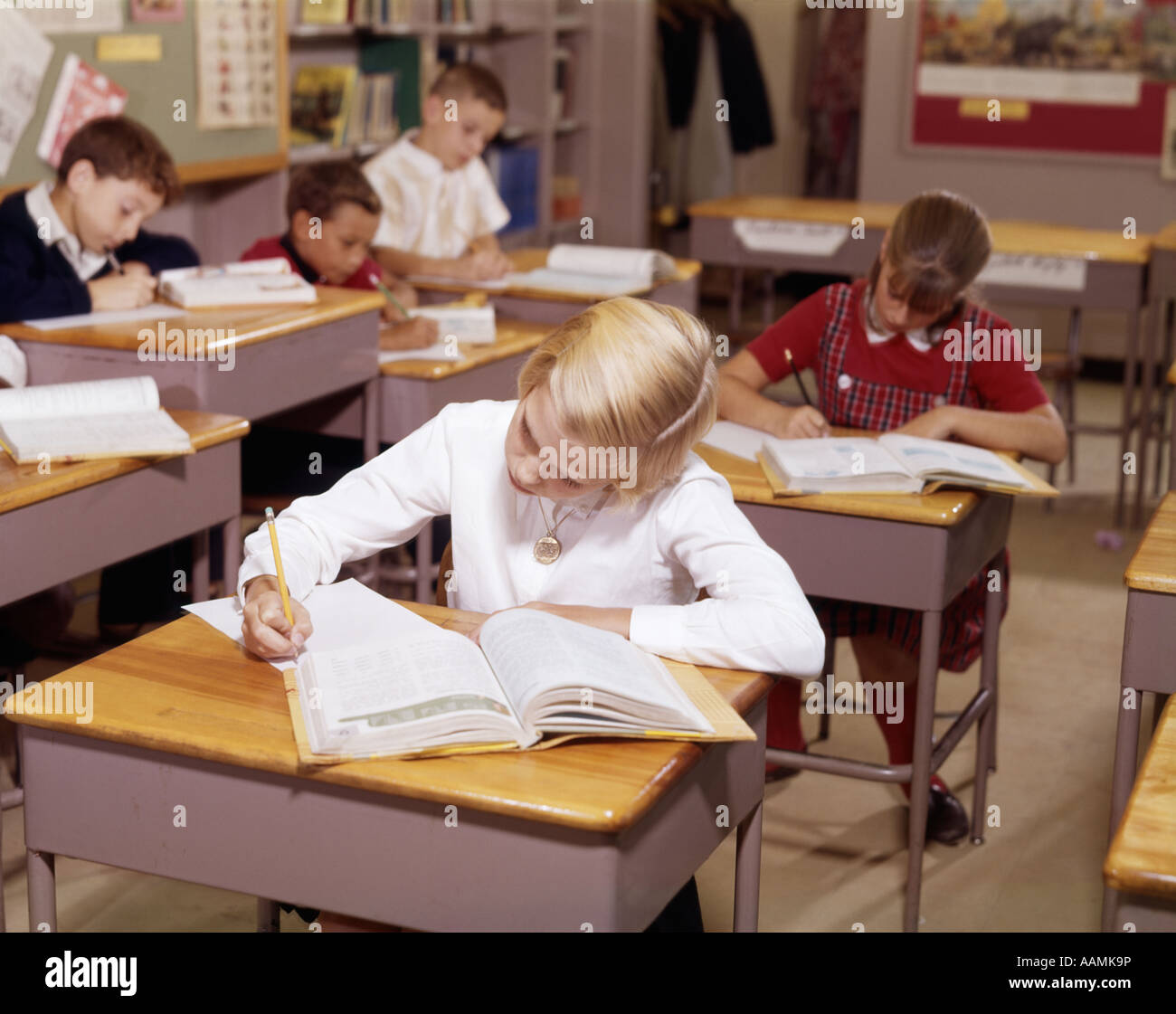 1960s ELEMENTARY SCHOOL CHILDREN IN CLASSROM AT DESKS WORKING WITH BOOKS AND PAPERS BOY GIRL Stock Photo