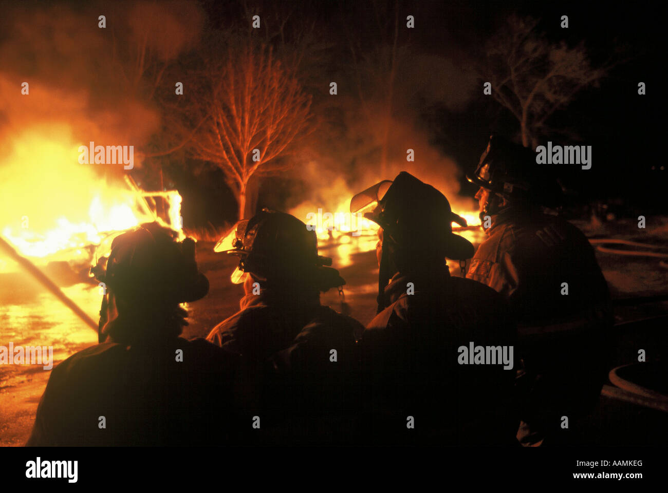 A group of fire fighters in front of a house on fire Stock Photo