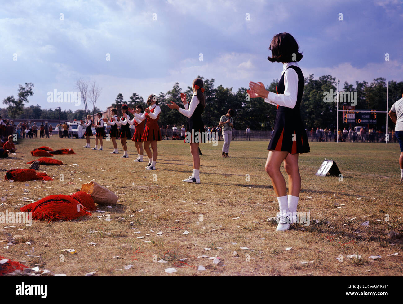 1960s LINE TEEN GIRL CHEERLEADERS ON SIDELINES CHEERING DURING HIGH SCHOOL FOOTBALL GAME UNIFORM SUPPORT PRIDE Stock Photo