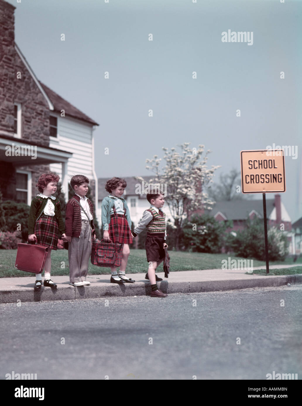 1950s 4 KIDS BOYS GIRLS SIDEWALK ABOUT CROSS STREET SCHOOL CROSSING SIGN HOUSE COMMUNITY SUBURBAN NEIGHBORHOOD Stock Photo