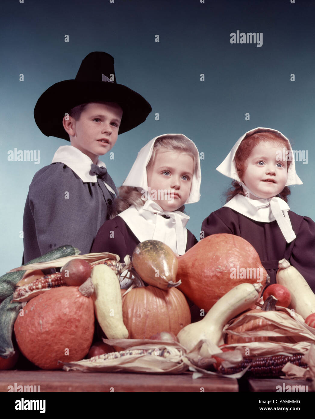 1950s 3 CHILDREN 2 GIRLS 1 BOY DRESSED IN PURITAN PILGRIMS COSTUMES PUMPKIN HARVEST VEGETABLES IN FOREGROUND Stock Photo