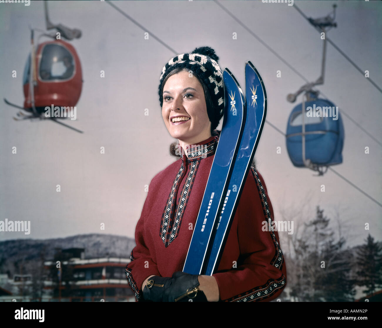 1970 1970s RETRO WOMAN IN WINTER GEAR HAT HOLDING SKIS SKI LIFT IN BACKGROUND Stock Photo