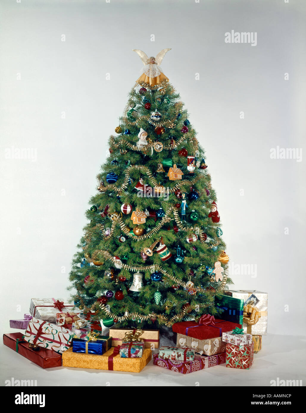 1950s 1960s 1970s COLORFUL DECORATED CHRISTMAS TREE SURROUNDED BY PRESENTS STUDIO INDOOR Stock Photo