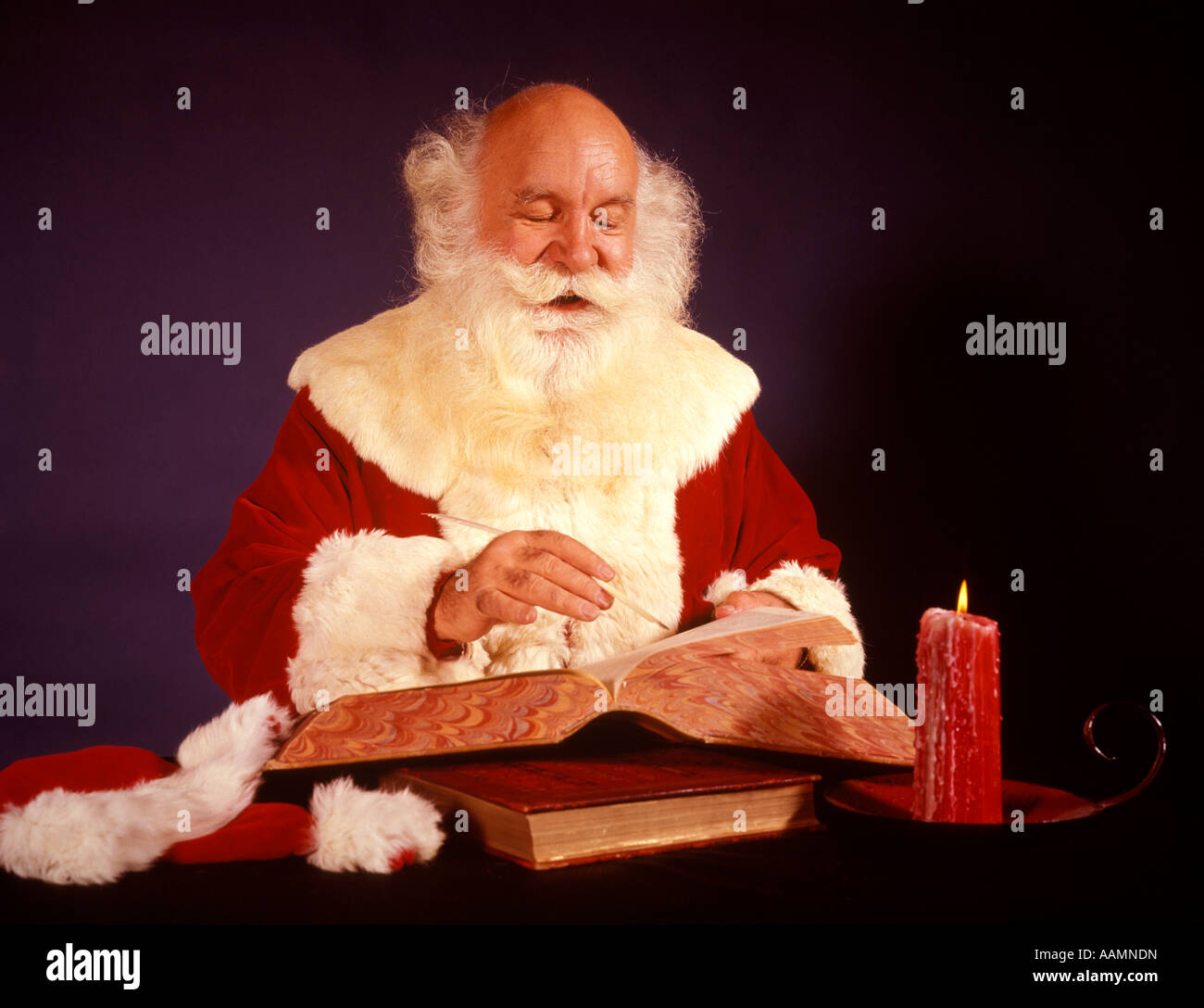 1950s 1960s 1970s BALD SANTA CLAUS WRITING LIST IN BIG BOOK BY CANDLE LIGHT STUDIO INDOOR Stock Photo