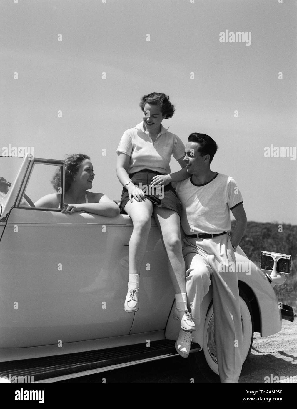 1930s GROUP OF FRIENDS SITTING WITH CONVERTIBLE ROADSTER AUTOMOBILE TALKING TOGETHER AT SEASHORE Stock Photo