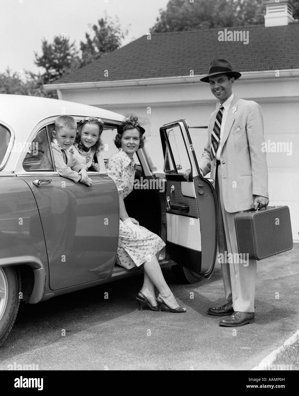 1950s MAN FATHER HOLDING SUITCASE AND OPENING AUTOMOBILE DOOR FOR WOMAN MOTHER DAUGHTER AND SON IN BACK SEAT Stock Photo