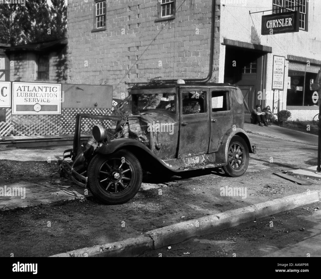 1920s WRECKED CAR SITTING ON SIDEWALK NEXT TO MECHANIC'S SHOP Stock Photo