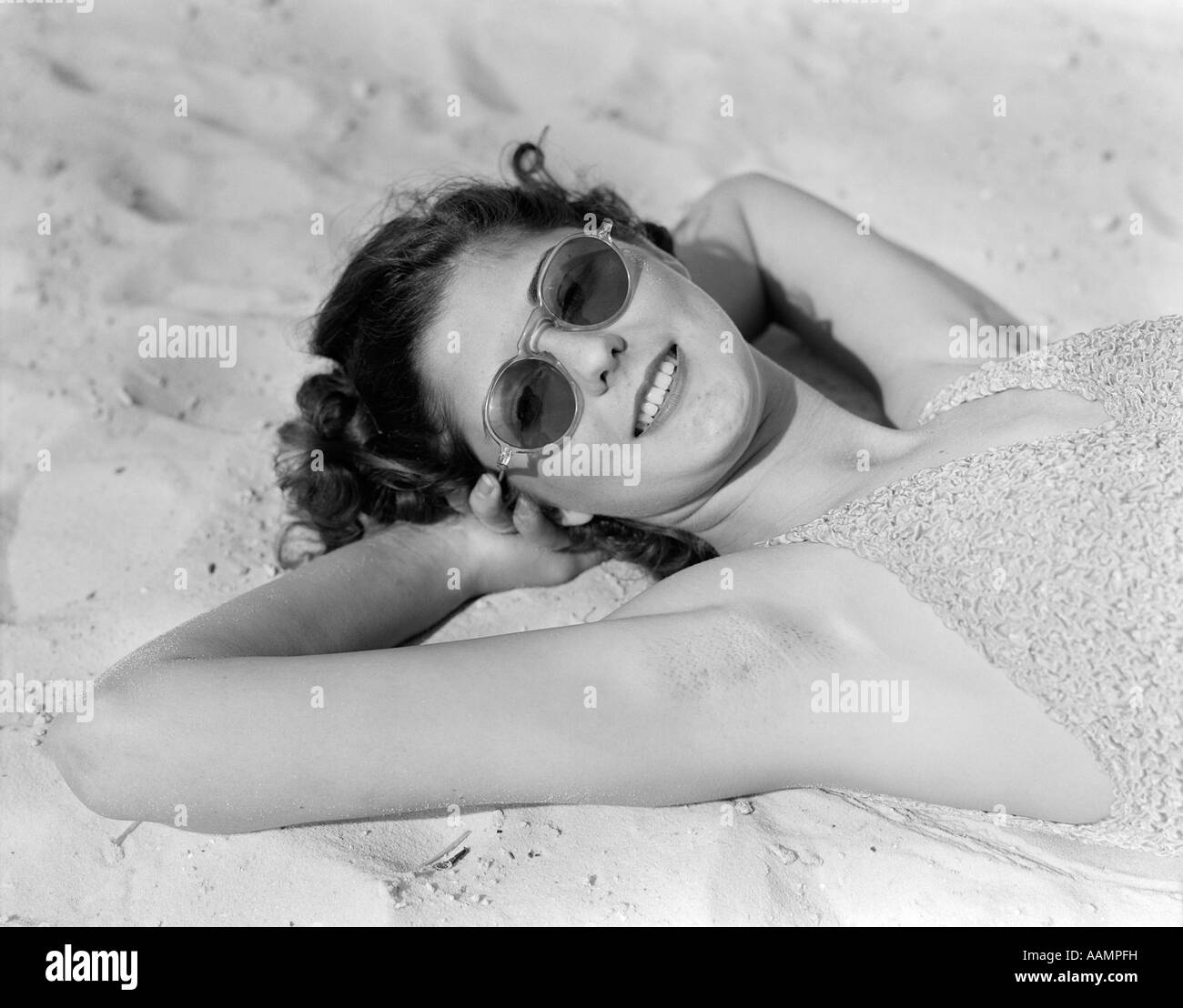 1930s WOMAN IN SUNGLASSES LYING ON BEACH WEARING BATHING SUIT Stock Photo
