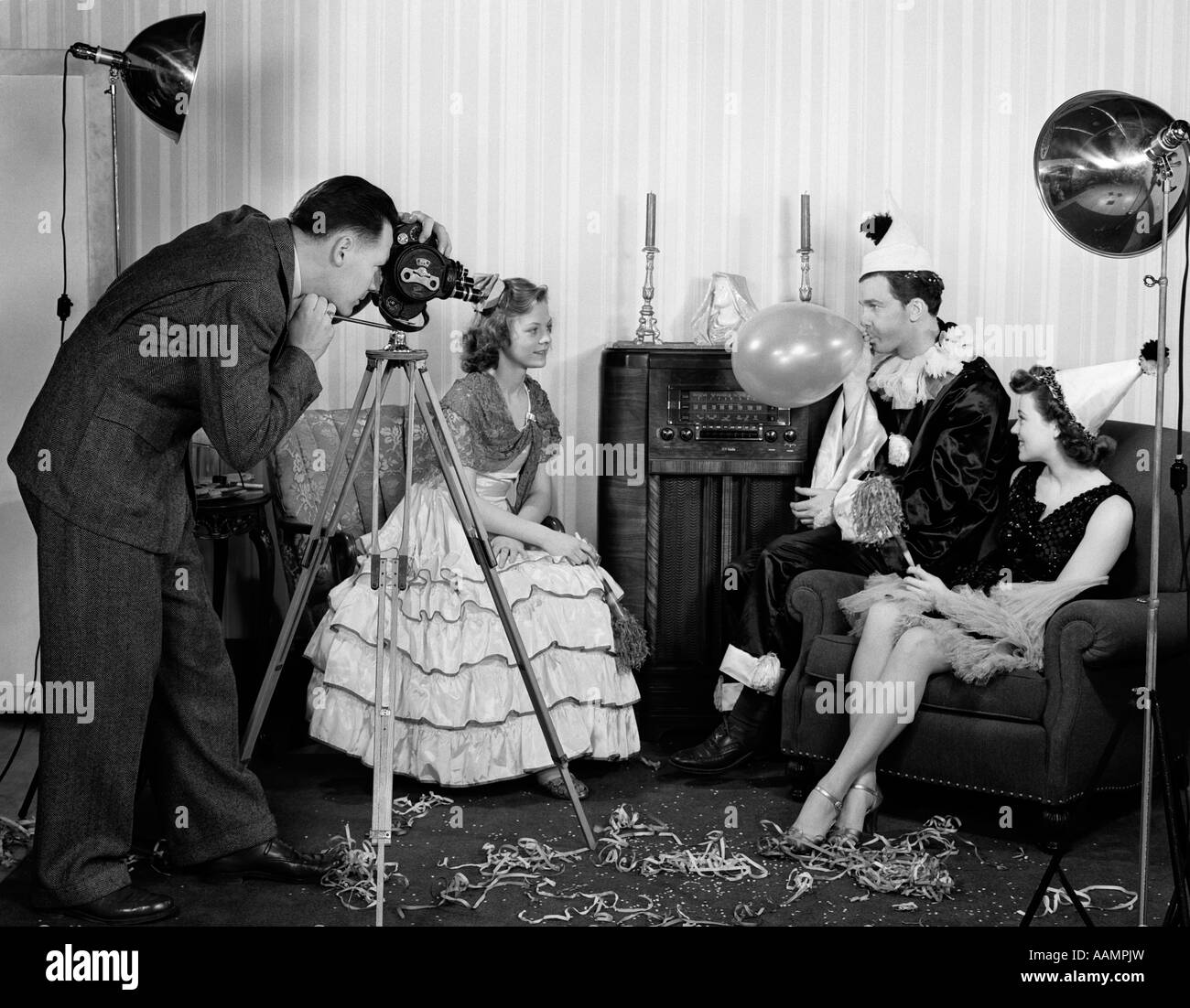 1940s PHOTOGRAPHER TAKING PICTURE OF TWO WOMEN & A MAN WEARING COSTUMES MAN BLOWING UP BALLOON Stock Photo
