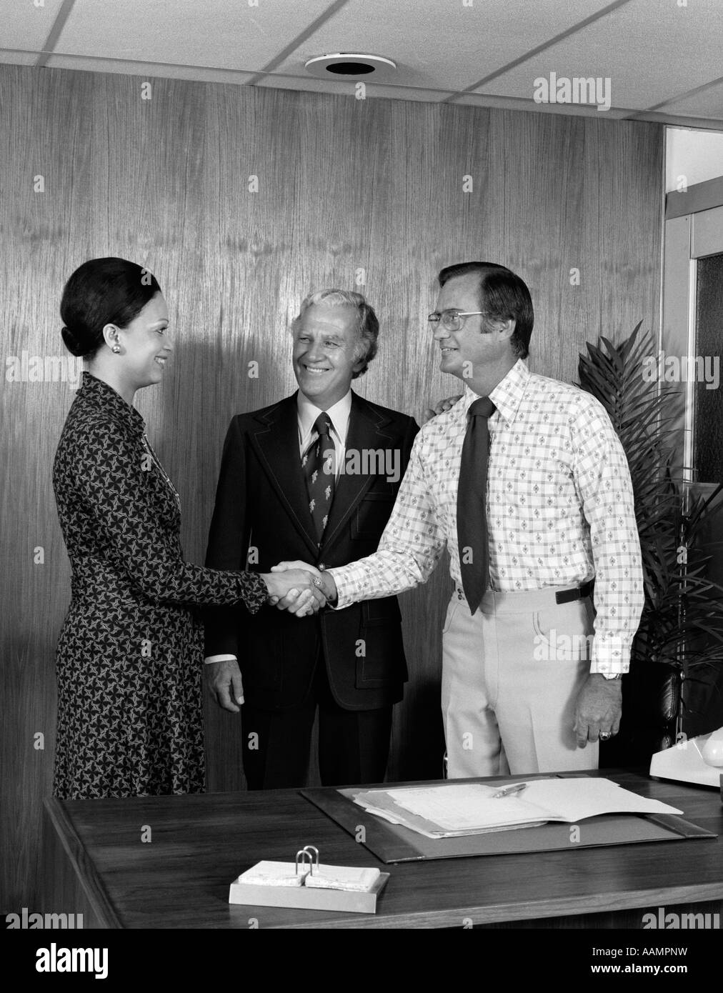 1970s 2 MEN ONE AFRICAN AMERICAN WOMAN SHAKING HANDS AGREEMENT AT BUSINESS MEETING Stock Photo