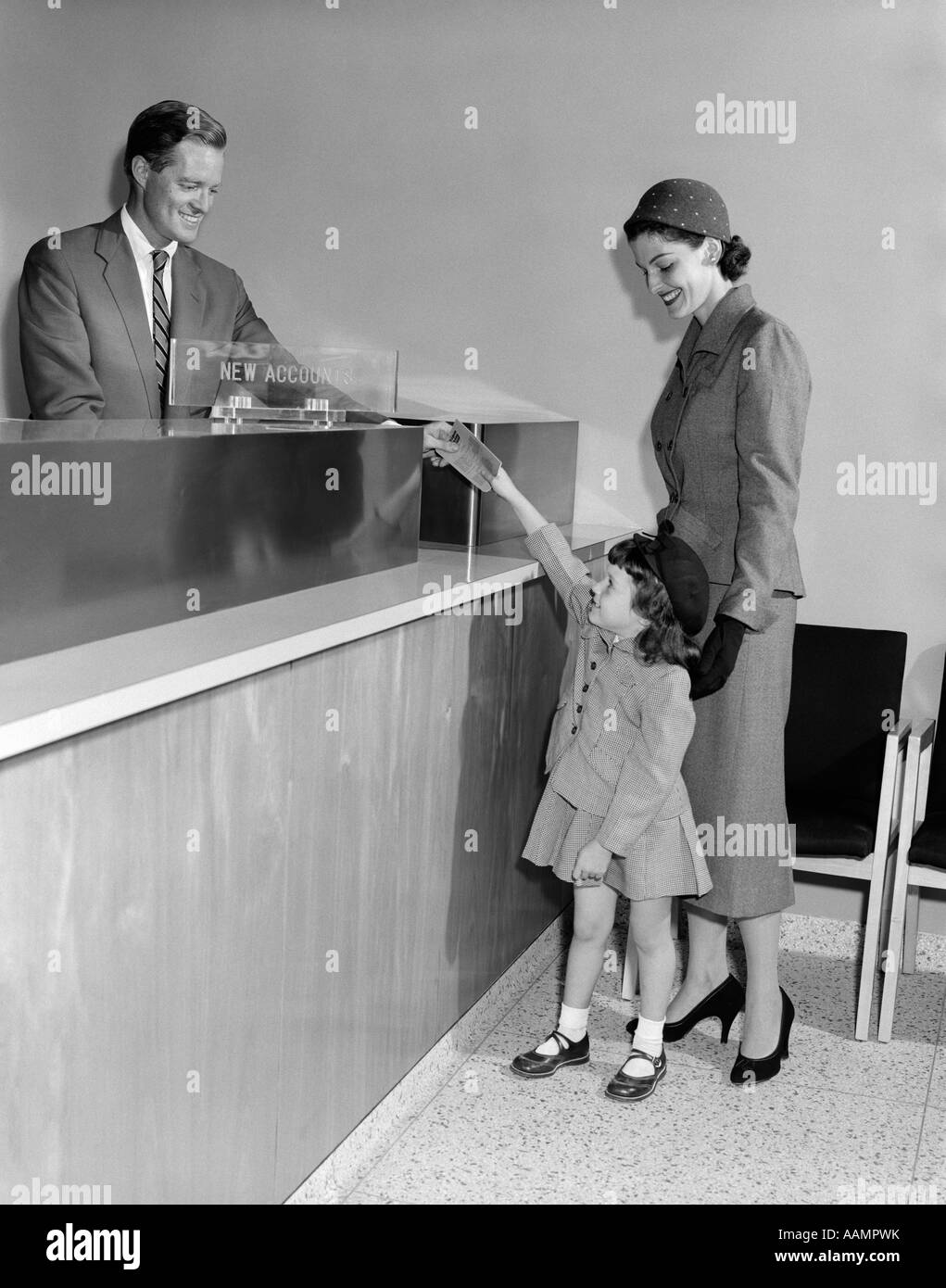 1950s MAN TELLER NEW ACCOUNTS IN BANK MOTHER WOMAN WITH LITTLE GIRL DAUGHTER HANDS PASSBOOK Stock Photo