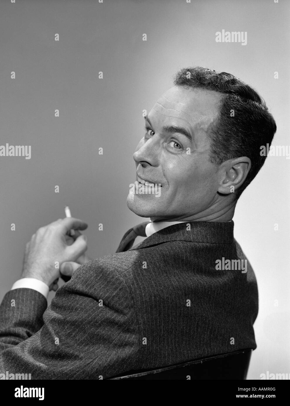 1950s 3 4 PROFILE MAN LOOKING OVER HIS SHOULDER CIGARETTE IN HAND SMILING Stock Photo