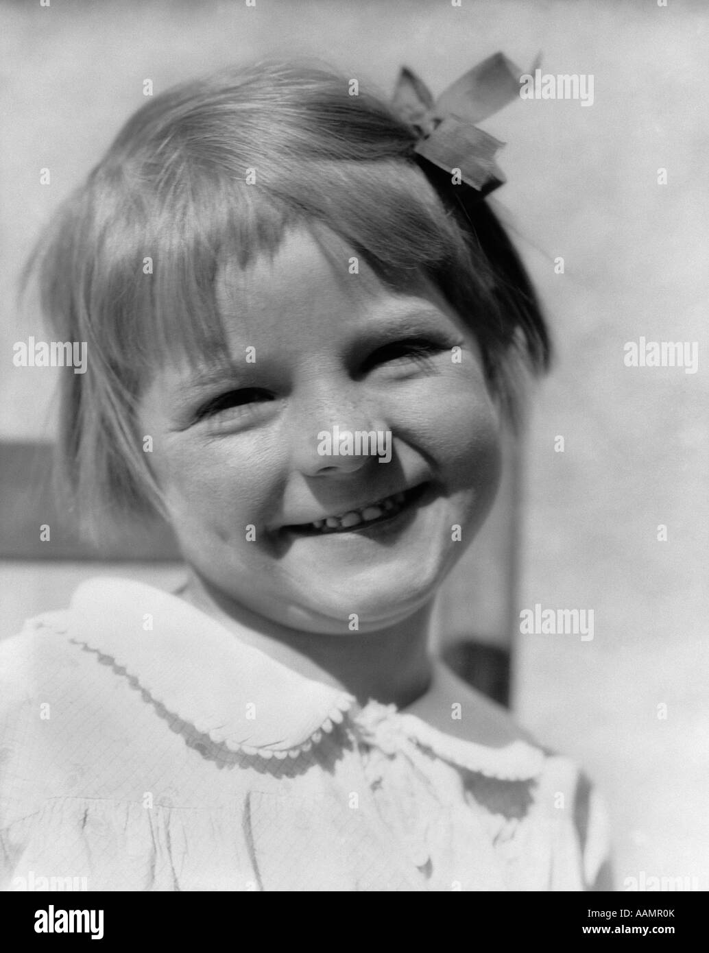 1930s YOUNG GIRL OUTDOOR PORTRAIT WITH FRECKLES AND BOW IN HAIR SMILING AT CAMERA Stock Photo