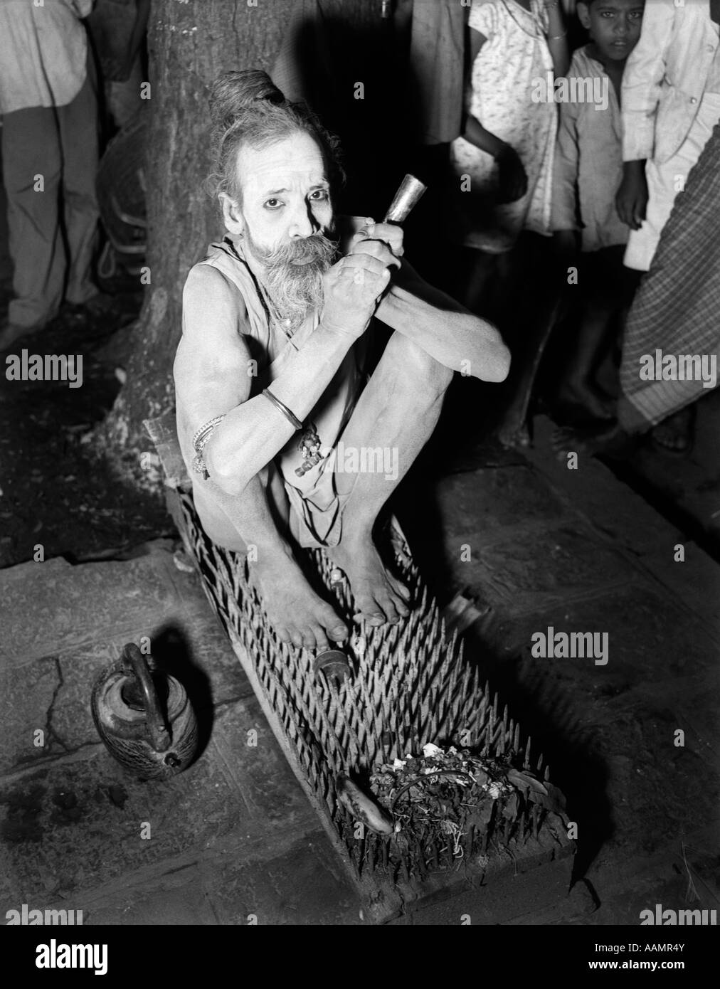 1930s HINDU HOLY MAN FAKIR SITTING ON BED OF SPIKES AND NAILS BOMBAY INDIA Stock Photo