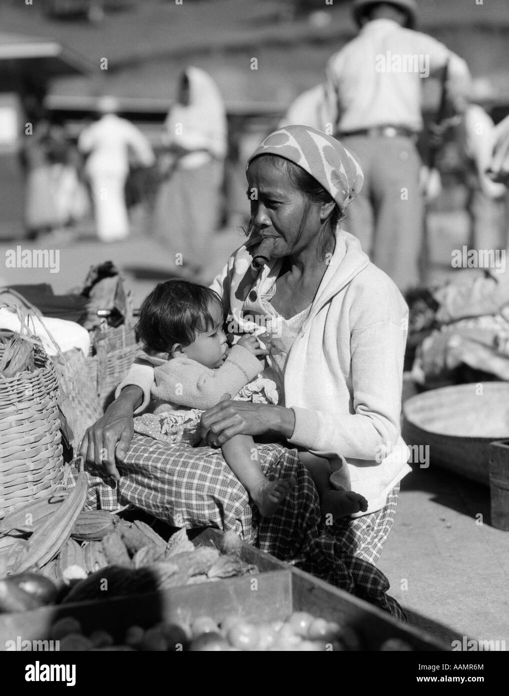 1920s 1930s MOTHER SITTING HOLDING BABY CHILD NURSING IN MARKET PLACE WOMAN SMOKING CIGAR CHEROOT BAGUIO PHILIPPINES Stock Photo