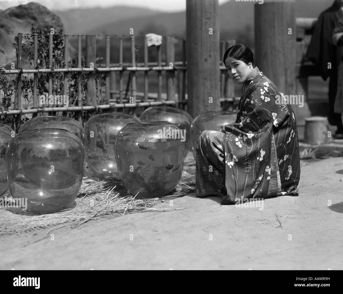 1930s UNSMILING JAPANESE WOMAN IN KIMONO KNEELING BY GROUP LARGE GOLD FISH BOWLS STREET GOLDFISH MARKET IN KOBE JAPAN Stock Photo