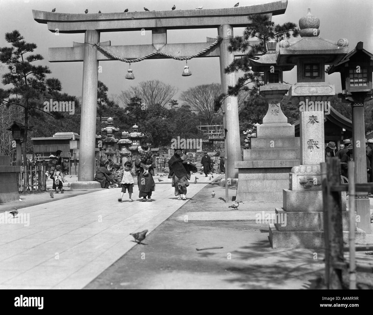 1930s WOMEN CHILDREN WALKING UNDER TORII GATE ARCH AT MINATOGAWA SHINTO SHRINE RELIGION GATEWAY KOBE JAPAN Stock Photo