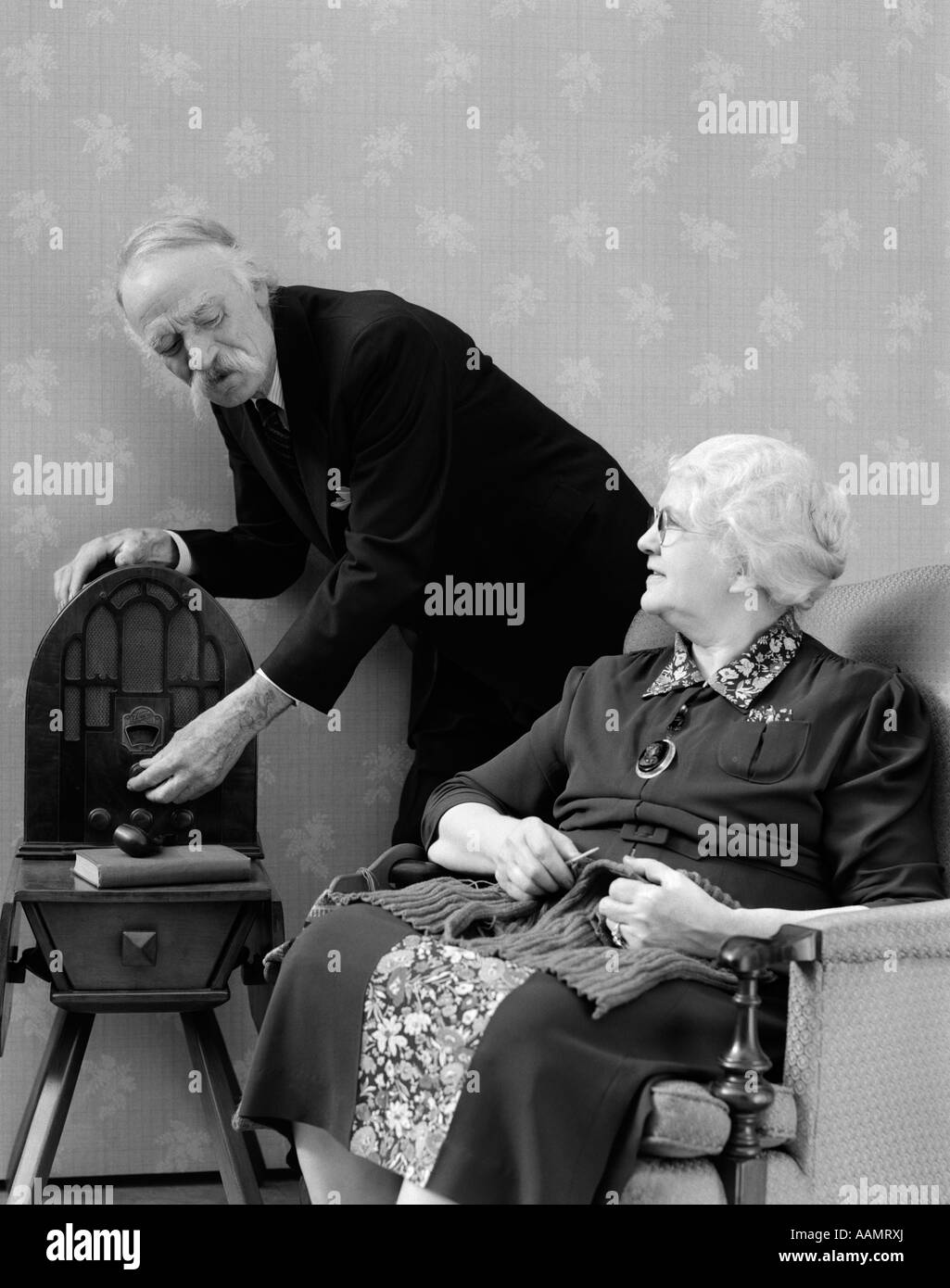 1940s ELDERLY COUPLE LISTENING TO RADIO WHILE SHE KNITS Stock Photo