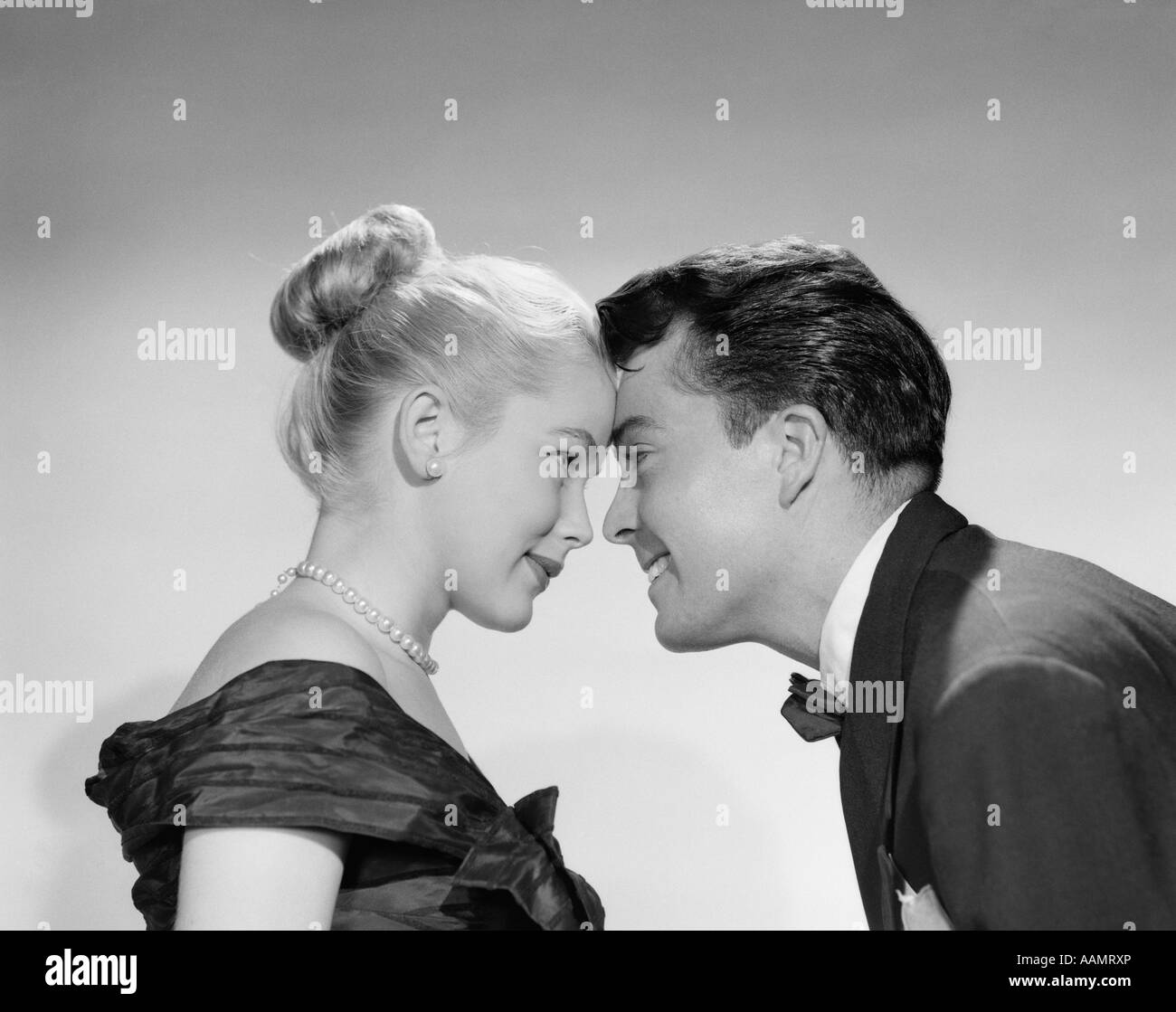 1950s MAN WOMAN COUPLE FOREHEADS TOUCHING PROFILE FORMAL ATTIRE TUXEDO PEARLS SMILING NOSE TO NOSE DATE FLIRT Stock Photo