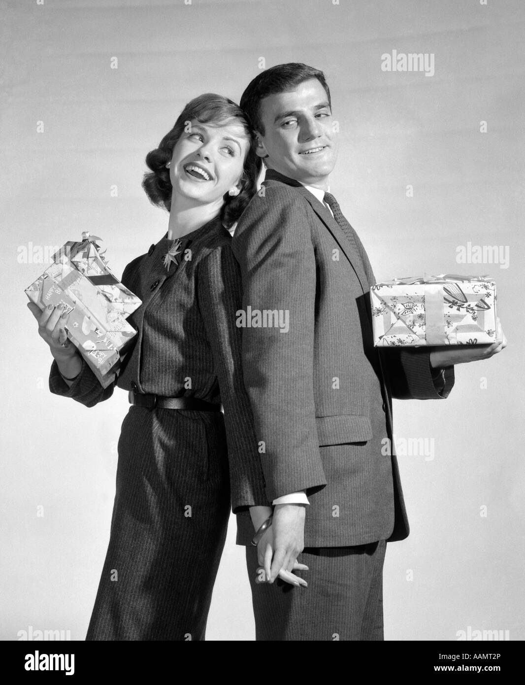 1950s COUPLE STANDING BACK TO BACK HOLDING HANDS AND PRESENTS Stock Photo