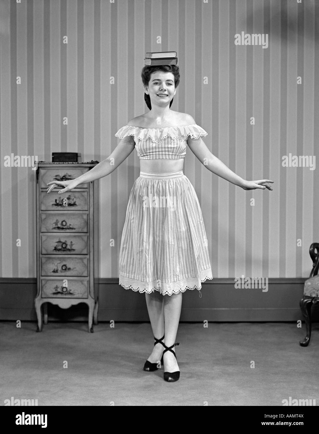 1940s 1950s YOUNG WOMAN IN DRESS BALANCING BOOKS ON HEAD Stock Photo