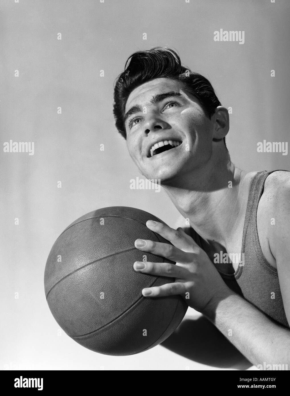 1950s PORTRAIT TEEN BOY MAN SMILING LOOKING UP HOLDING BASKETBALL PLAYER Stock Photo