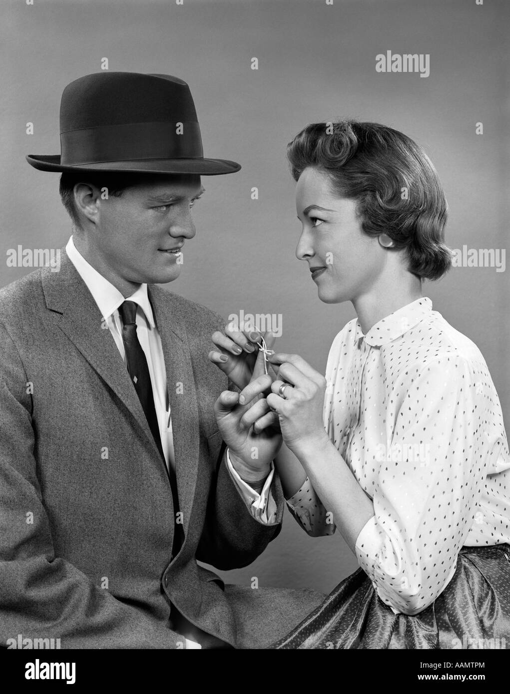 1950s COUPLE WOMAN TYING A STING IN A BOW AROUND MAN'S FINGER AS A REMINDER TO DO SOMETHING Stock Photo