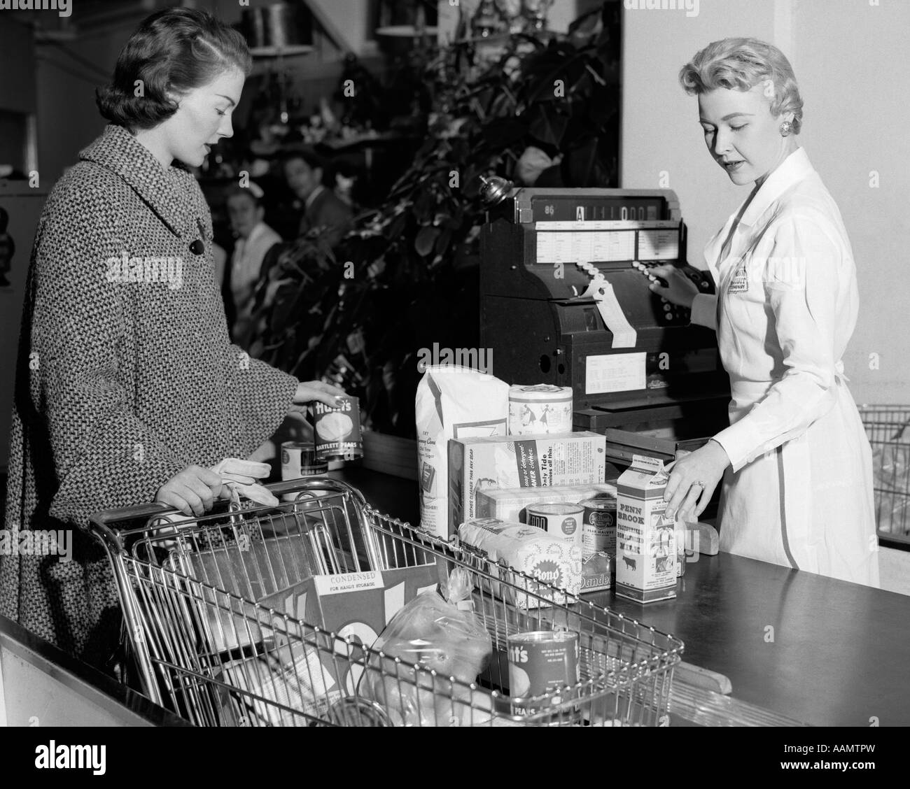 1950s WOMAN AT GROCERY STORE CHECKOUT COUNTER HANDING ITEMS OVER FOR - 1300x1129 - jpeg Store Register Check Out