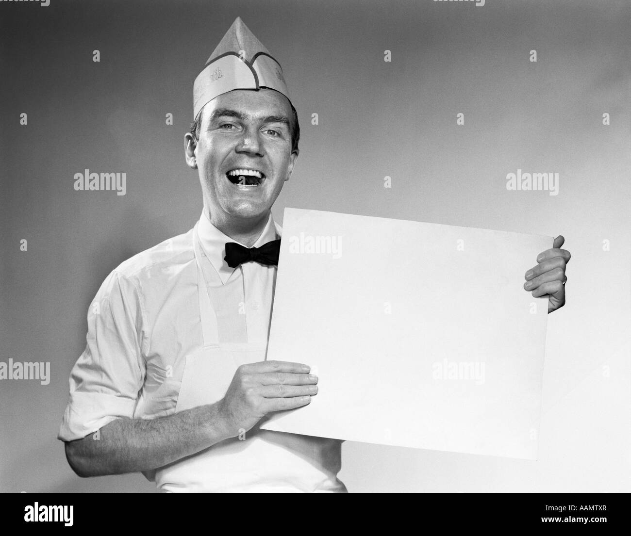 1950s 1960s HAPPY MAN IN WHITE SERVICE UNIFORM HOLDING BLANK SIGN LOOKING AT CAMERA Stock Photo