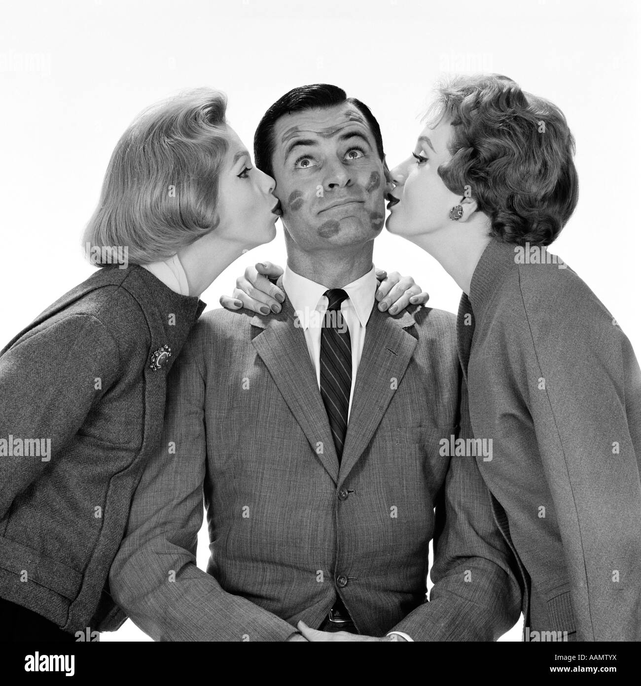 1950s TWO WOMEN KISSING SINGLE MAN ON OPPOSITE CHEEKS HIS FACE COVERED WITH LIPSTICK MARKS Stock Photo